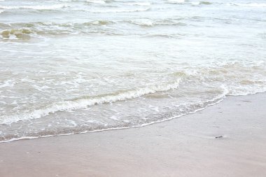 Kum kıyısında küçük deniz dalgaları. Fotoğraf sıcak, bulutlu bir sonbahar gününde çekildi..