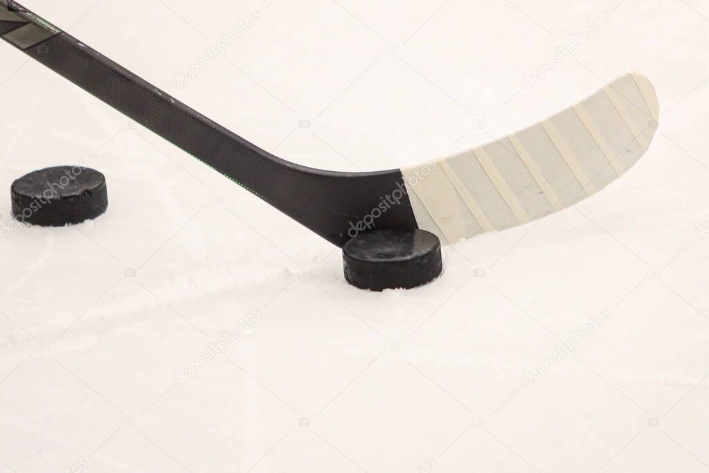 Ice hockey stick with black hockey puck near on ice details. Photo taken  on warmup before game.