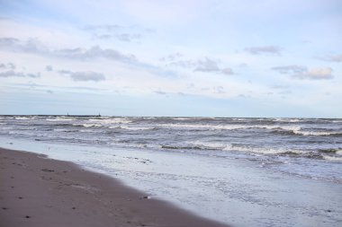 Baltık deniz kıyısı manzaralı, dalgalı ve bulutlu bir hava. Fotoğraf küçük bir deniz kentinde çekildi. Arka planda deniz feneri olan iskele.