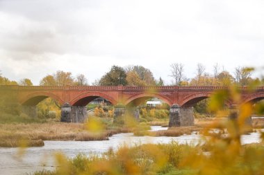 Letonya 'nın Kuldiga kentindeki Venta nehrinin üzerindeki eski kırmızı tuğlanın sonbahar manzarası. Fotoğraf sıcak, bulutlu bir sonbahar gününde çekildi..