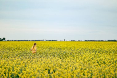 Bahar mevsiminde canlı kanola tarlasında oynayan oldukça uzun saçlı bir kız.