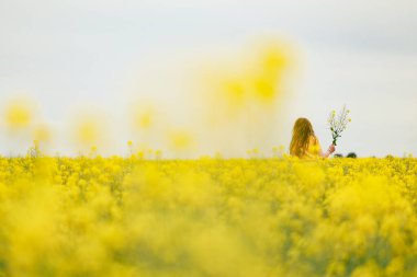 Bahar mevsiminde canlı kanola tarlasında oynayan oldukça uzun saçlı bir kız.