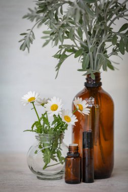 Kasımpatı çiçekleri beyaz arka planda kehribar esanslı yağ şişeleriyle sergileniyor