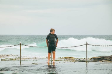 Newcastle, New South Wales Avustralya 'daki Bogey Hole' da dalgalar çarptığında çitlere tutunan çocuk.