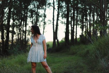 Ormanda uzun kahverengi saçlı, yaz elbisesi giyen bir kadın.