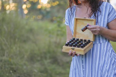 Firefly NSW Australia - 20 April 2022: Woman standing in field holding wooden storage box full of doterra essential oils clipart
