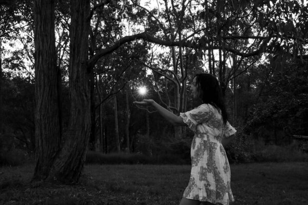 Black and white image of woman in the woods at sunset holding sunburst in the palm of hand