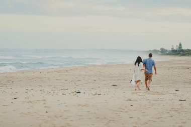 Üç kişilik küçük bir aile sahilde köpeklerle birlikte yürüyor.