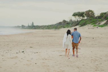 Üç kişilik küçük bir aile sahilde köpeklerle birlikte yürüyor.