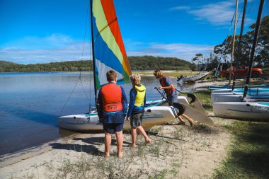 Smith Gölü, NSW Avustralya - 29 Nisan 2022: Çocuklar güneşli bir günde köpüklü kahve kayıkhanesinde yelkencilik dersine katılıyor