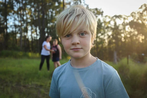 Sarışın, beyaz bir çocuk. Arka planda annesi ve kardeşiyle sarmaş dolaş.