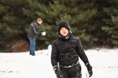 Babasıyla karda oynayıp arka planda kardan adam yapan mutlu çocuk.