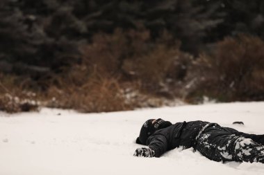 Genç çocuk karda sırt üstü yatıyor.
