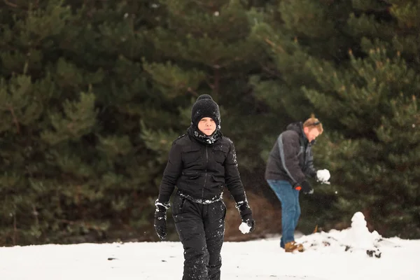 Babasıyla karda oynayıp arka planda kardan adam yapan mutlu çocuk.