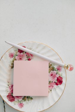 Gül kalemi ve beyaz arka planda orkide çiçekleri ile çiçek plakası üzerine pembe yapışkan not düz yatıyordu