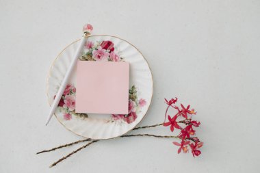 Gül kalemi ve beyaz arka planda orkide çiçekleri ile çiçek plakası üzerine pembe yapışkan not düz yatıyordu