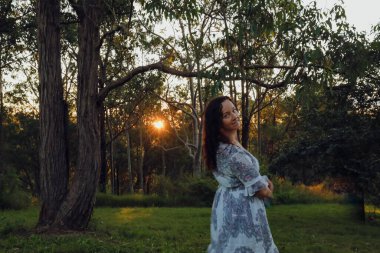 Gün batımında ormanda bir kadın Ağaçların arasından parlayan güneş ışığıyla