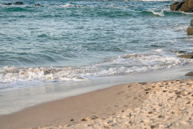 Kumsalda hafif dalgalar kırılıyor yumuşak kumda ayak izleri var, yakından kesilmiş.