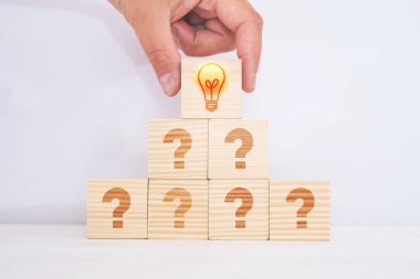 Yaratıcı fikir ve yenilik kavramı. Piramidin tepesinde bir ampul ikonu ve soru işareti sembolüyle eşleştirilmiş tahta küp bloğu