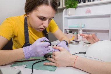 Eldivenli usta bir kız, bir müşterinin manikürcüdeki tırnaklarına şeffaf bir temel uygular. Çivi bakımı kavramı