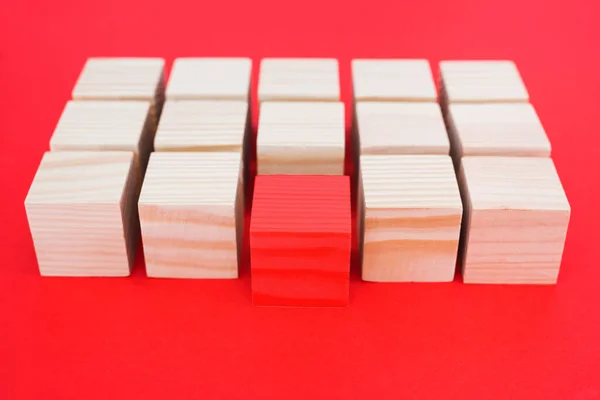 One other red cube block among wooden blocks on a red background. The concept of individuality, leadership and uniqueness