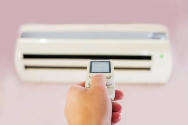 Odanın içinde kadın kontrol paneliyle klima var. Uzaktan kumandalı klima.