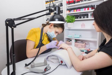 Güzellik Salonu, Manikür, Çivi Cila Prosedürü. Güzellik salonunda elektrikli makine kullanan profesyonel donanım manikürü. Usta manikür sırasında ojeli elleri kesmek için elektrikli makine kullanıyor..