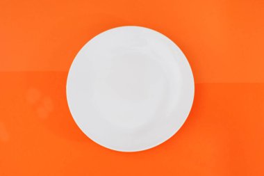 Turuncu arka planda boş beyaz plaka. Yukarıdan görüntüle.