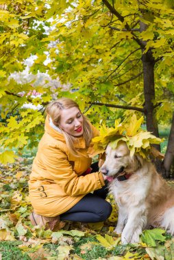 Sarı sonbahar yaprakları arasında av köpeği olan sarı ceketli genç bir kadın.