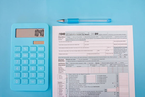 tax form 1040 with calculator and pen on blue background. Financial document. View from above.