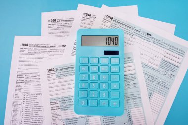 Vergi 1040 formunda mavi bir hesap makinesi ve mavi bir arkaplan. Yukarıdan bak. Mali belgeler.