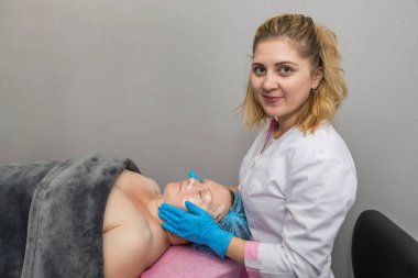 Mavi lastik eldivenli profesyonel bir dermatolog. Orta yaşlı, sorunlu bir kadın hastaya film uyguluyor. Yüz bakımı kavramı