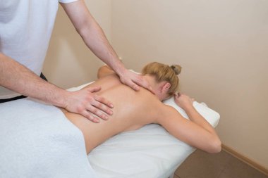 Spa salonunda masaj yatağında yatan çekici bir kadın. Erkek masör genç kıza sırt masajı yapıyor.