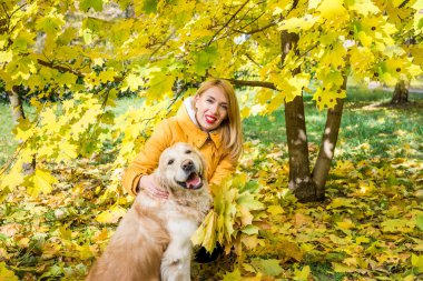 Sarı sonbahar yaprakları arasında av köpeği olan kalın elbiseli bir kadın.
