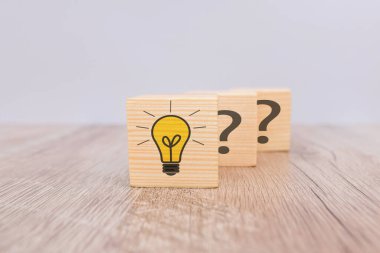 Yaratıcı fikir ve yenilik kavramı. Ampul simgesi ve soru işareti sembollü tahta küp bloğu