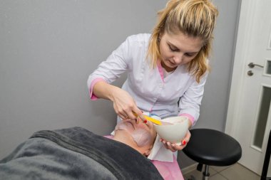 Jöleli aljinat maskesini bir kadının yüzünden çıkarma süreci. Yüz yenileme prosedürü. Güzellik salonunda cilt bakımı