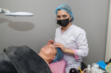Profesyonel bir kadın kozmetik uzmanı müşterisine elle masaj yapar. Spa salonundaki yüz bakımı, kozmetoloji prosedürleri.