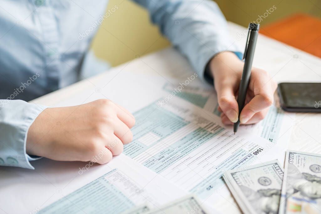 Close-up of a woman filling out a 1040 form while sitting at a table. Tax concept, financial document
