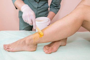 Güzellik salonunda şekerleme işlemi. Kozmetik uzmanı kadın epilasyon ya da tüy dökme işleminden önce genç kızın bacağına balmumu ya da şeker sürüyor.. 