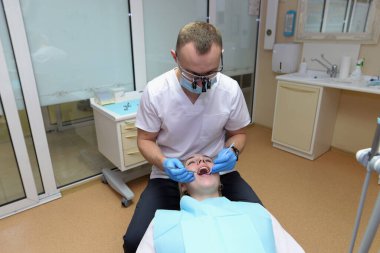 Erkek dişçi dişçi dişçi muayenehanesinde genç bir kıza bakar.