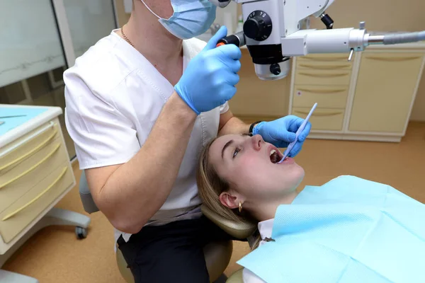 男性歯科医は若い美しい女性を調べ 手術室でプロの顕微鏡で彼女の歯を見て — ストック写真