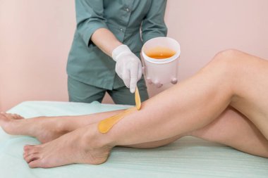 Glikoz macunu kullanılarak bacaklarda epilasyon işlemi. Spa merkezinde kozmetik şeker saçı kesimi.