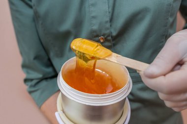 Ahşap bir çubuğa tüy dökmek için sıvı sarı şeker yapıştırıcısı ya da ağda. Güzellik uzmanının elinde karıştırmak için şeker ezmesi..