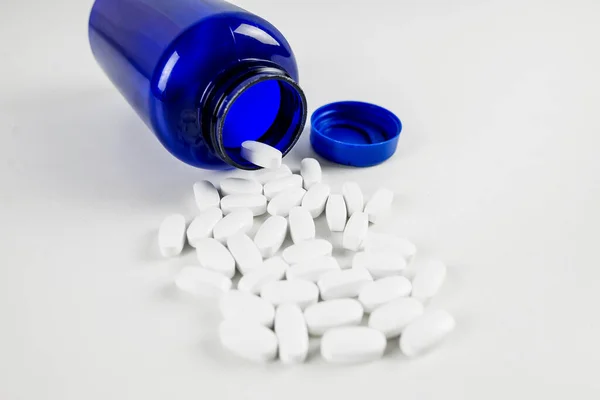 Kék Palack Fehér Tablettákkal Fehér Asztal Hátterén Közelkép — Stock Fotó