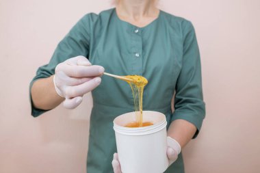 Güzellik uzmanı bir kadın elinde şeker ezmesi tutuyordu. Spa stüdyosunda saç kesimi. Titreyen kadın bacaklarının balmumu tüy dökümü.