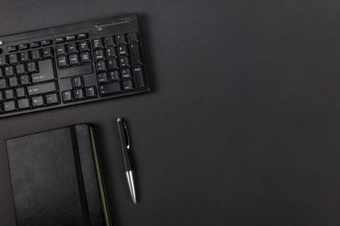 Siyah klavyenin üst görünümü, siyah not defteri ve kopya alanı olan siyah arkaplan üzerindeki kalem.
