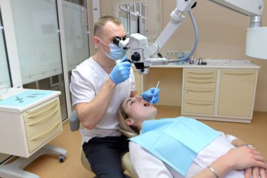 Doktor dişçi bir hastanın dişlerini mikroskop altında tedavi eder.