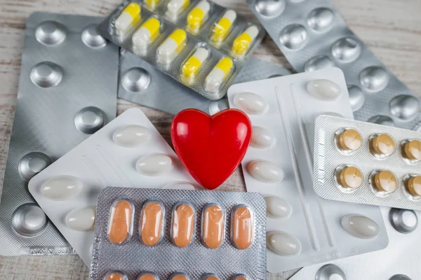 Farklı hapların arka planında kırmızı kalp. Kardiyovasküler hastalık kavramı.