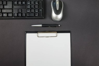 Siyah arkaplan üzerinde klavye, fare, kalem ve hesap makinesi olan ofis panosunun en üst görünüm fotoğrafı
