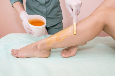 Güzellik uzmanı bir güzellik salonunda bir kadının bacaklarının şeker macununu tükürür. Kadın estetik kozmetolojisi.